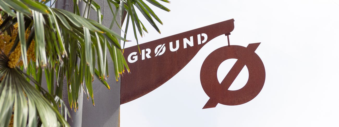 Insegna Ground in metallo corten tra le palme